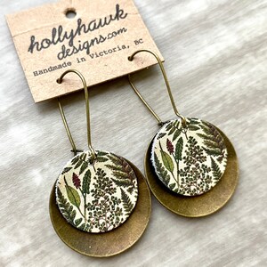 May include: A pair of gold tone earrings with a round, white and green floral pattern on the front. The earrings are handmade in Victoria, BC by hollyhawkdesigns.com.