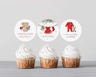 Könnte beinhalten: Drei Cupcakes mit runden Aufsätzen mit weihnachtlichen Babyparty-Designs. Die Aufsätze zeigen Babykleidung, ein Kleid und einen Strampler. Der Text enthält "Stephanie & Tyler's baby shower", "santa baby" und "welcome baby Carter".