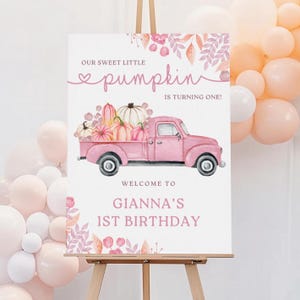 May include: A pink sign on an easel with the text "Our Sweet Little Pumpkin is Turning One!" and "Welcome to Gianna's 1st Birthday." A pink truck carries pumpkins. Balloons are in the background.