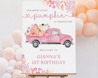 May include: A pink sign on an easel with the text "Our Sweet Little Pumpkin is Turning One!" and "Welcome to Gianna's 1st Birthday." A pink truck carries pumpkins. Balloons are in the background.