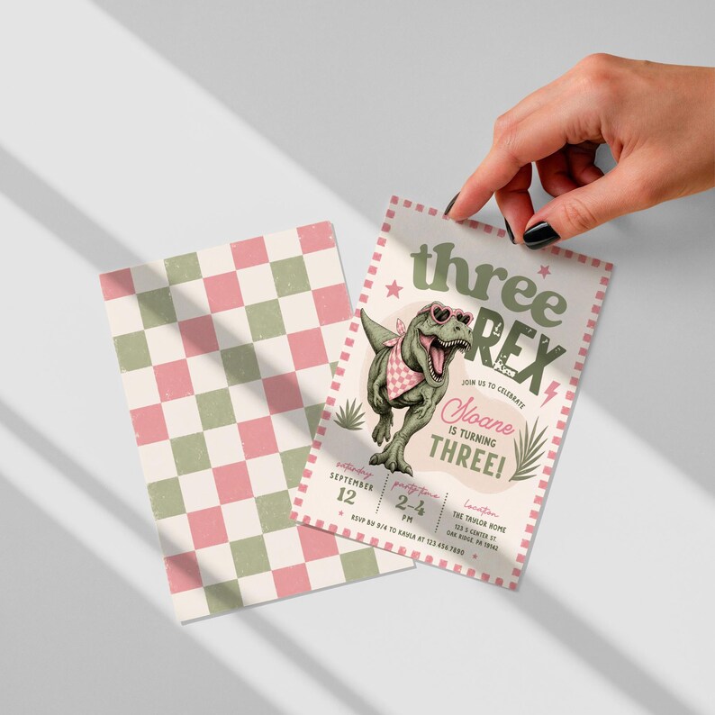 May include: A rectangular birthday invitation card featuring a green T-Rex wearing pink heart-shaped sunglasses and a checkered bandana. The text reads three REX, Noane is turning THREE, and party details. A matching pink and green checkered card is included.