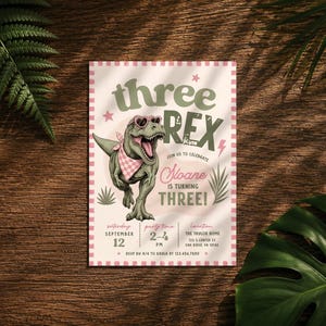 May include: A rectangular birthday invitation card featuring a green T-Rex wearing heart-shaped sunglasses and a pink checkered bandana. The text reads: three REX, join us to celebrate Sloane is turning THREE, Saturday September 12, 2-4 PM, The Taylor Home.
