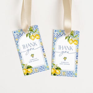 May include: Two rectangular gift tags with a blue and white tile pattern border. The tags feature a lemon and floral design with the words "THANK you" and "ISABELLA'S BABY SHOWER". Each tag is attached to a beige ribbon.