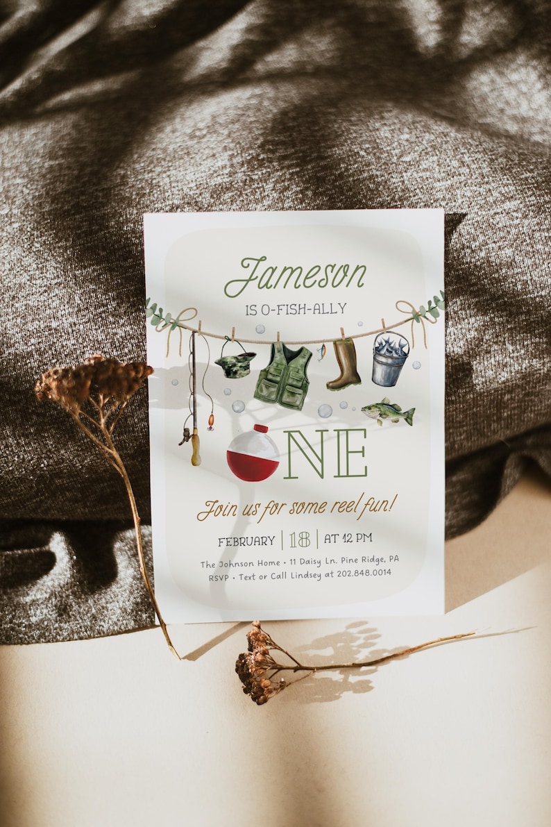 May include: A fishing-themed first birthday party invitation with a green and brown color scheme. The invitation features a watercolor illustration of fishing gear, including a fishing rod, a life vest, a bucket, and a fish. The text on the invitation reads "Jameson is O-Fish-Ally One" and includes the date and time of the party.