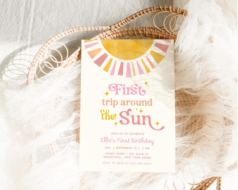 May include: A cream-colored invitation card with a sun design in pink, yellow, and orange. The text reads "First trip around the Sun" and announces Ella's First Birthday. The card includes date, time, and location details.