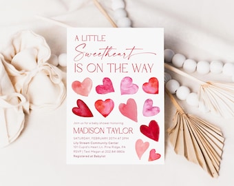 May include: A baby shower invitation with the text "A Little Sweetheart Is On The Way." The invitation features watercolor hearts in shades of red and pink. Details include the honoree's name, date, time, and location.