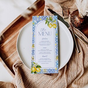 Puede incluir: Una tarjeta de men&uacute; con un dise&ntilde;o de azulejos azules y blancos, con limones y el texto "the MENU". El men&uacute; enumera entrantes, platos principales y postres. La tarjeta est&aacute; en un plato blanco.