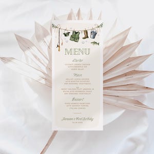 Könnte beinhalten: Eine druckbare Speisekarte mit einem Angel-Thema. Die Speisekarte umfasst eine Vorspeise, ein Hauptgericht, ein Dessert und einen Hinweis auf "Jaceman's 1st Birthday". Die Karte ist mit Illustrationen von Angelausrüstung verziert, darunter eine Angelrute, eine Schwimmweste, ein Angelstiefel, ein Eimer und ein Fisch.