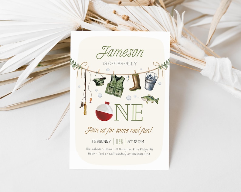 May include: A light beige invitation card with a fishing theme. The card says "Jameson is O-Fish-Ally One" with a fishing rod, a life vest, boots, a bucket of fish, and a fish hanging on a clothesline. The text also says "Join us for some reel fun!" with the date and time of the event, the location, and contact information.