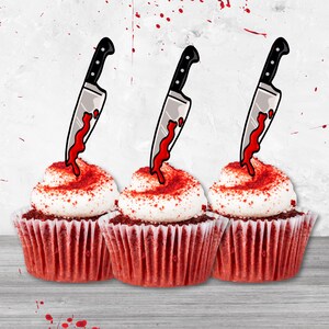 以下が含まれることがあります： 赤いベルベットのカップケーキ3つ。白いフロスティングがかけられ、黒いナイフが乗っています。ナイフの刃から赤い液体が垂れています。