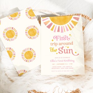 May include: Two invitations with a sun theme. One invitation has a repeating pattern of yellow and pink suns on a white background. The other invitation has the text "First trip around the Sun" with event details. The invitations are in a woven basket.