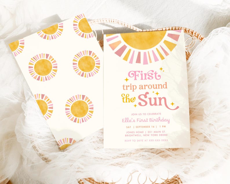 May include: Two invitations with a sun theme. One invitation has a repeating pattern of yellow and pink suns on a white background. The other invitation has the text "First trip around the Sun" with event details. The invitations are in a woven basket.