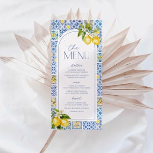 May include: A rectangular menu card with a blue and white tile pattern border. The menu features the text "the MENU" at the top, with a list of starters, main courses, and desserts. Lemon illustrations and floral accents decorate the card.