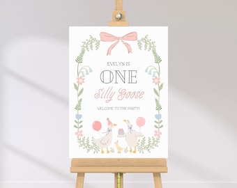 Puede incluir: Una corona floral rosa y verde con un lazo rosa en la parte superior rodea el texto "Evelyn is One Silly Goose" y un mensaje de bienvenida a la fiesta. Dos gansos de dibujos animados con globos están debajo del texto.