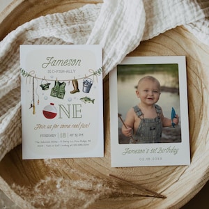 May include: A birthday invitation for a boy named Jameson turning one year old. The invitation features a fishing theme with a red and white fishing bobber, a green fishing vest, a fishing rod, a bucket, and a fish. The invitation text reads "Jameson is O-Fish-Ally One" and "Join us for some reel fun!" The invitation also includes the date, time, and location of the party. A photo of Jameson holding a fishing rod is included in the invitation.