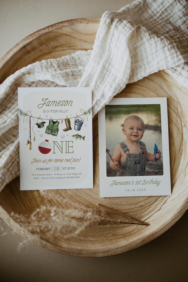 May include: A birthday invitation for a boy named Jameson turning one year old. The invitation features a fishing theme with a red and white fishing bobber, a green fishing vest, a fishing rod, a bucket, and a fish. The invitation text reads "Jameson is O-Fish-Ally One" and "Join us for some reel fun!" The invitation also includes the date, time, and location of the party. A photo of Jameson holding a fishing rod is included in the invitation.