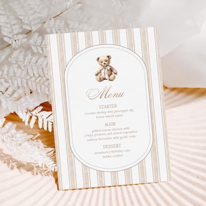 Op de afbeelding: Een menukaart met een teddybeer-illustratie. De kaart heeft een beige en witte gestreepte achtergrond. Het menu bevat voorgerechten, hoofdgerechten en desserts. De menu-items zijn in een sierlijk lettertype geschreven.