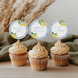 Puede incluir: Tres cupcakes con glaseado marr&oacute;n claro y adornos decorativos. Los adornos son redondos con un dise&ntilde;o de azulejos azules y blancos, ilustraciones de limones y texto que dice "la dolce VITA", "ISABELLA'S baby shower" y "Ciao BABY!"