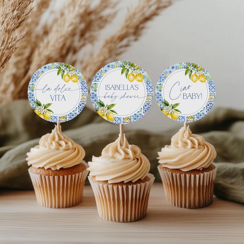 Puede incluir: Tres cupcakes con glaseado marr&oacute;n claro y adornos decorativos. Los adornos son redondos con un dise&ntilde;o de azulejos azules y blancos, ilustraciones de limones y texto que dice "la dolce VITA", "ISABELLA'S baby shower" y "Ciao BABY!"