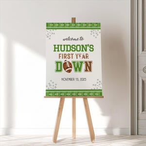 Puede incluir: Un cartel de bienvenida blanco con acentos verdes y marrones. El cartel dice "Bienvenido a Hudson's First Year Down" con un gr&aacute;fico de f&uacute;tbol y la fecha "13 de noviembre de 2025".
