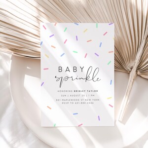 Puede incluir: Una invitaci&oacute;n de baby shower blanca con un patr&oacute;n de chispas de colores y el texto "Baby sprinkle" en letra cursiva negra. La invitaci&oacute;n incluye el nombre "Brinley Taylor", la fecha "Sun | August 20 | 1 PM", la direcci&oacute;n "801 Maplewood St New York" y el n&uacute;mero de RSVP "601-680-2246".