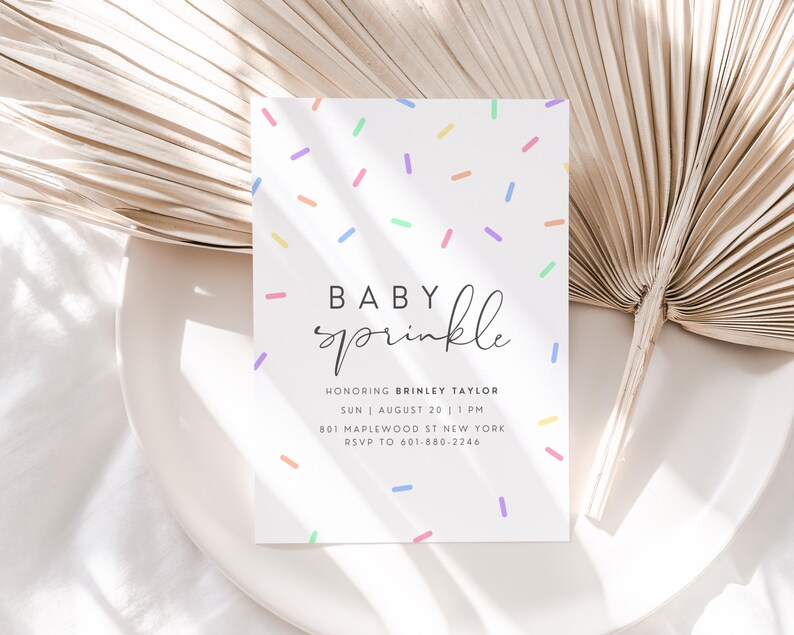 Puede incluir: Una invitaci&oacute;n de baby shower blanca con un patr&oacute;n de chispas de colores y el texto "Baby sprinkle" en letra cursiva negra. La invitaci&oacute;n incluye el nombre "Brinley Taylor", la fecha "Sun | August 20 | 1 PM", la direcci&oacute;n "801 Maplewood St New York" y el n&uacute;mero de RSVP "601-680-2246".