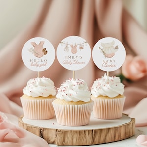 Peut inclure: Trois cupcakes roses et blancs avec du glaçage et des pépites. Chaque cupcake est surmonté d'un rond en papier avec un motif et du texte sur le thème du bébé. Les toppers disent "Hello baby girl", "Emily's Baby Shower", et "Baby Carter".