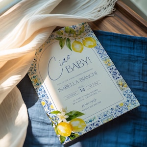 Könnte beinhalten: Babyparty-Einladung mit Zitronen- und Blumendesign. Die Einladung lautet "Ciao BABY!" und enthält Details für die Babyparty von Isabella Bianchi, einschließlich Datum, Uhrzeit und Ort. Die Einladung ist mit einem blau-weißen Fliesenmuster verziert.