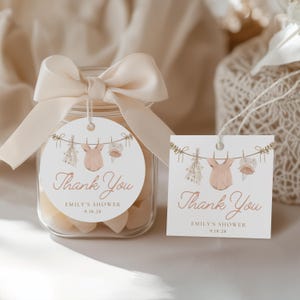 May include: Two round thank you tags with a pink baby onesie hanging on a clothesline with flowers and a teddy bear. The text on the tags reads "Thank You Emily's Shower 9.18.28".
