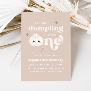May include: A beige invitation card with a cute cartoon dumpling illustration. The text reads "Our little dumpling is turning one" and includes details for a first birthday party.