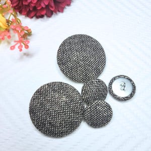 May include: Four brown and white fabric covered buttons of different sizes. The buttons are round and have a textured surface.