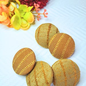 May include: Five round, brown fabric buttons with a gold striped pattern.
