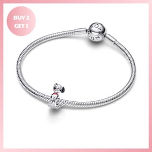 Könnte beinhalten: Ein silbernes Schlangenkettenarmband mit einem runden Verschluss, der mit dem Wort PANDORA graviert ist, und einem kleinen Anhänger in Form eines gefleckten Hundes mit rotem Halsband. Das Armband wird mit einer Grafik mit dem Text BUY 2 GET 1 gezeigt.