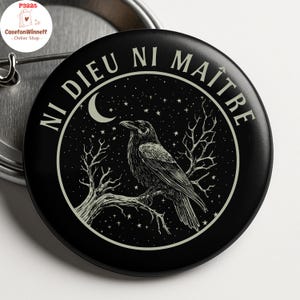 May include: Black button featuring a raven on a branch, with a night sky and crescent moon design. The text "NI DIEU NI MAITRE" is in a circle around the raven. The button has a pin back.