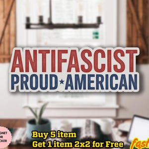 May include: A sticker with the words "ANTIFASCIST PROUD AMERICAN" in red and blue, with a white border. The sticker is rectangular and features a star. The background is blurred, showing a window and a table.