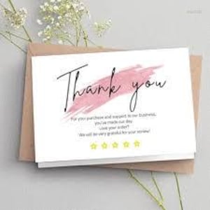 May include: A white card with the words "Thank you" in black script, accented by a pink brushstroke. The card includes additional text and four yellow stars, resting on a brown envelope.
