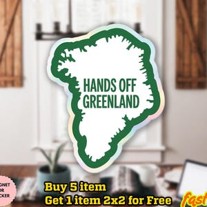 May include: A white sticker in the shape of Greenland with a green outline and the text "HANDS OFF GREENLAND". The sticker has a holographic border and is displayed on a window.