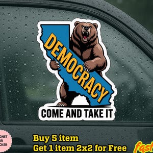 May include: A sticker featuring a brown bear holding a blue sign in the shape of California with the word "DEMOCRACY" in yellow. The text "COME AND TAKE IT" is below the bear. The sticker is on a car window.