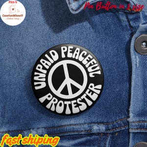 May include: A black button pin with white text that reads "UNPAID PEACEFUL PROTESTER" around a white peace symbol. The pin is on a blue denim jacket. The text "Pin Button in 3 size" is in red at the top.