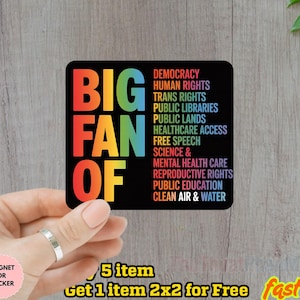 May include: A black square sticker with the words "BIG FAN OF" in rainbow colors. Below, a list of social and political issues is printed in white. The sticker is held by a hand.