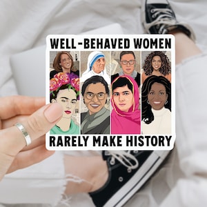 May include: A rectangular sticker featuring illustrations of notable women, with the text "WELL-BEHAVED WOMEN RARELY MAKE HISTORY." The sticker includes portraits of several women. The sticker is held by a hand.