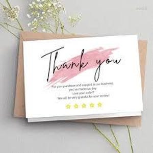 May include: A white card with the words "Thank you" in black script, accented by a pink brushstroke. The card includes additional text and four yellow stars, resting on a brown envelope.