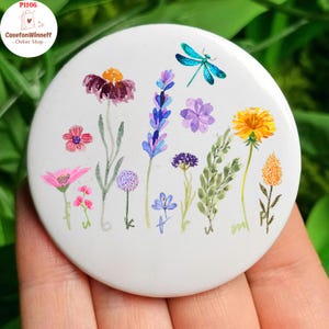 May include: A white button with a watercolor floral design featuring various flowers and a teal dragonfly. The button has the text "CasetonWinett - Online Shop" and the product code "P1105" in a circular logo.