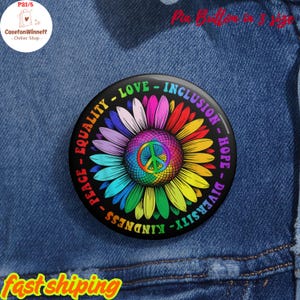May include: A round, black pin button with a colorful daisy design. The center features a peace symbol, surrounded by petals in rainbow hues. Text around the edge reads "LOVE - INCLUSION - HOPE - DIVERSITY - KINDNESS - EQUALITY - PEACE".