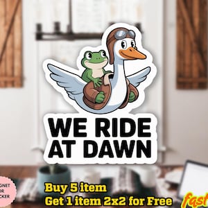 May include: A sticker featuring a cartoon goose wearing goggles and a frog riding on its back. The goose has a brown jacket and the text "WE RIDE AT DAWN" is below the image. The sticker is waterproof and can be used as a magnet.