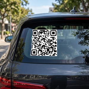May include: A square black and white QR code sticker applied to the rear window of a dark grey vehicle. The sticker features a high-contrast geometric pattern of black squares on a white background, centred on the glass surface of the car.