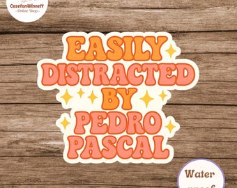 May include: A white sticker with the text "EASILY DISTRACTED BY PEDRO PASCAL" in orange and pink bubble letters. The sticker has a retro design with star accents. The sticker is waterproof.