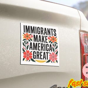 May include: A white square magnet or sticker with the text "IMMIGRANTS MAKE AMERICA GREAT" in black, surrounded by colorful floral illustrations. The magnet is affixed to a white vehicle.