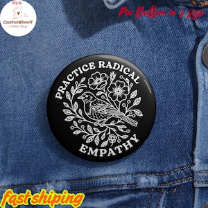 Könnte beinhalten: Schwarzer runder Ansteckbutton mit den weißen Worten "PRACTICE RADICAL EMPATHY", die eine weiße Illustration eines Vogels und eines floralen Designs umgeben. Der Button befindet sich auf einem blauen Jeanshintergrund.