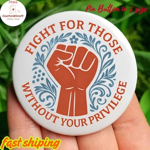 May include: A white pin button with the text "FIGHT FOR THOSE WITHOUT YOUR PRIVILEGE" in a circular design. The center features a raised fist in orange, surrounded by blue floral accents. The button is approximately 1.5 inches in diameter.